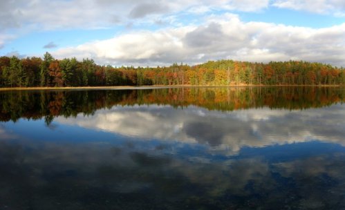 A serene lake reflecting colorful autumn trees and a cloudy sky, creating a peaceful natural landscape.