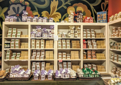 A colorful display of various packaged soaps on shelves, featuring different shapes and sizes, against a vibrant background.