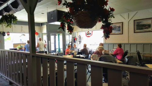A cozy restaurant interior with patrons dining, surrounded by plants and decorative flowers.