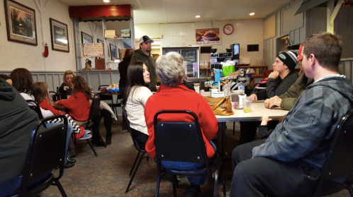 A cozy diner scene with people sitting at tables, chatting, and enjoying food in a casual atmosphere.