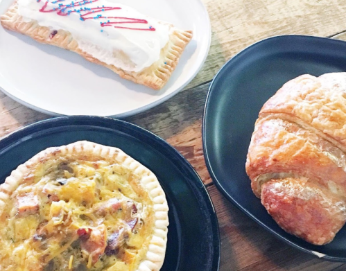 A plate with a frosted pastry, a savory pie, and a flaky croissant on a wooden table.