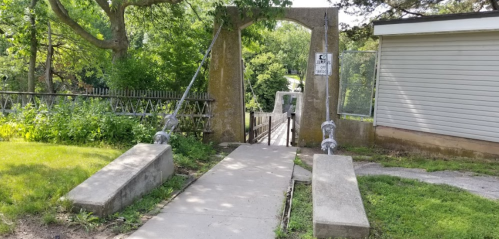 A concrete pathway leads to an archway surrounded by greenery, with a sign posted nearby.