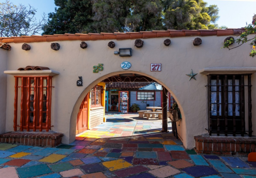 Colorful courtyard entrance with arched doorway, vibrant tiled floor, and buildings with decorative windows.