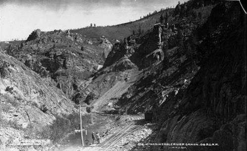 Black and white photo of a canyon with rocky cliffs and a railway track along a river.
