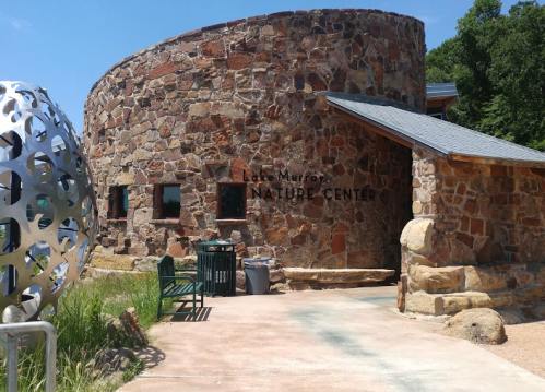 Stone building with "Lake Murray Nature Center" sign, surrounded by greenery and a modern sculpture nearby.