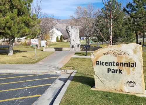 Sign for Bicentennial Park in North Ogden City, with trees and a pathway visible in the background.