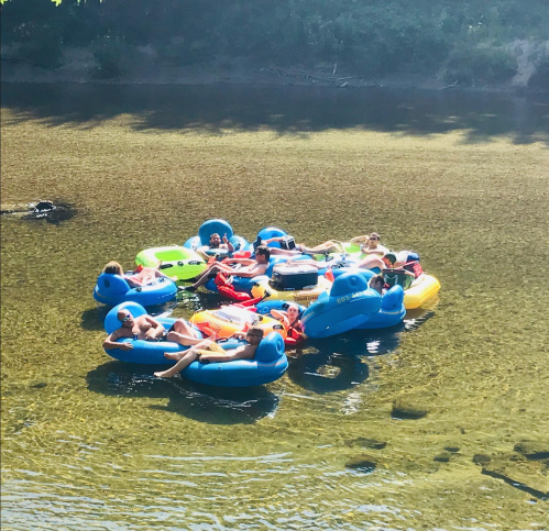 A group of people relaxing on colorful inflatable rafts in a shallow river on a sunny day.