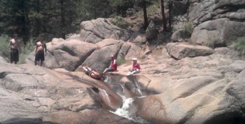 People enjoying a natural water slide on smooth rocks in a forested area.
