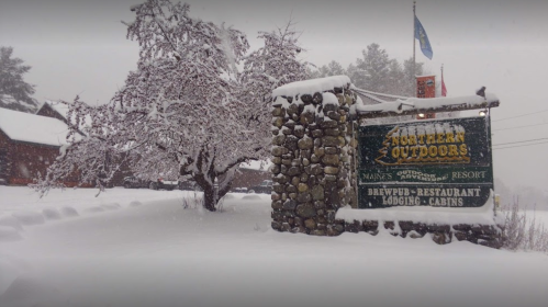 A snowy scene featuring a stone sign for Northern Outdoors, surrounded by trees and a winter landscape.