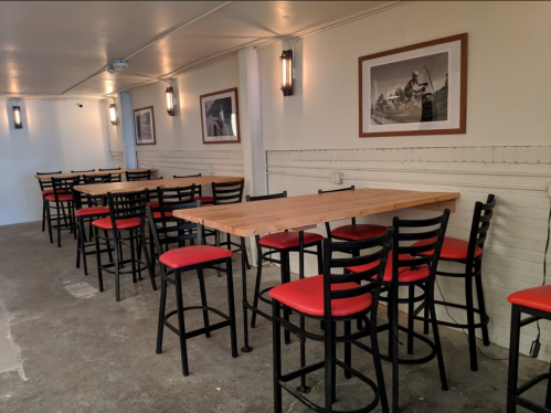 A spacious dining area with wooden tables and black chairs featuring red cushions, illuminated by wall sconces.