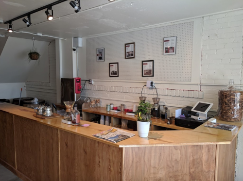 A wooden counter in a cafe with a coffee setup, plants, and framed photos on the wall.