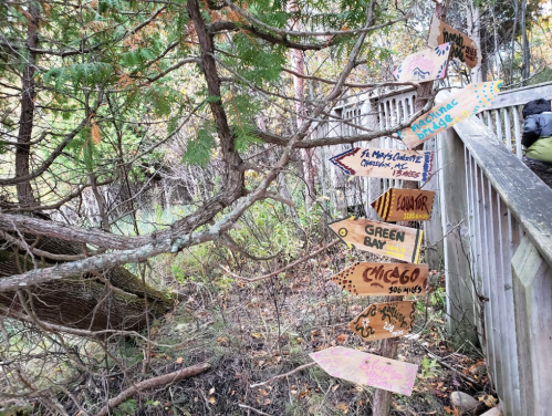 Wooden signposts with arrows pointing to various destinations, surrounded by trees and a wooden railing.