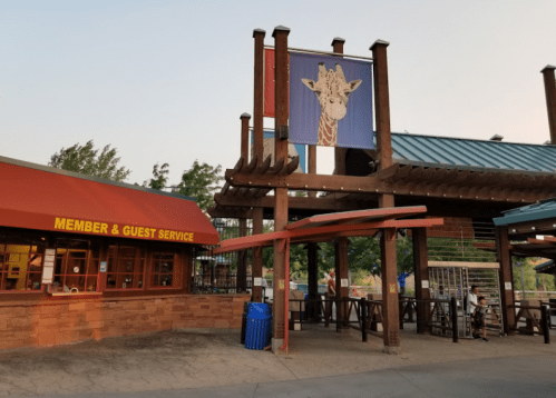 Entrance to a zoo featuring a giraffe banner and a guest services area with a red awning.