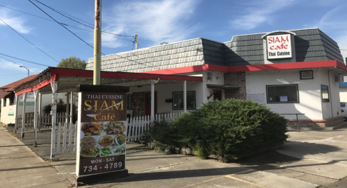 Exterior of Siam Cafe, a Thai restaurant, featuring a sign and a green bush in front under a clear blue sky.