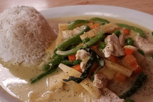 A plate of chicken stir-fry with vegetables in a creamy sauce, served with a side of white rice.