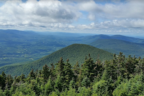 A panoramic view of lush green mountains under a partly cloudy sky, showcasing rolling hills and valleys.