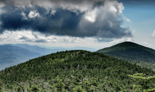 A panoramic view of lush green mountains under a cloudy sky, with rolling hills in the background.