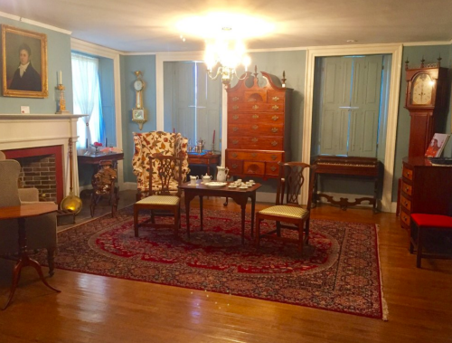 A cozy room with antique furniture, a chandelier, and a patterned rug, featuring a tea set on a table.