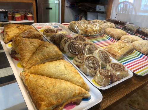 A display of assorted baked goods, including pastries, cinnamon rolls, and scones, arranged on colorful trays.