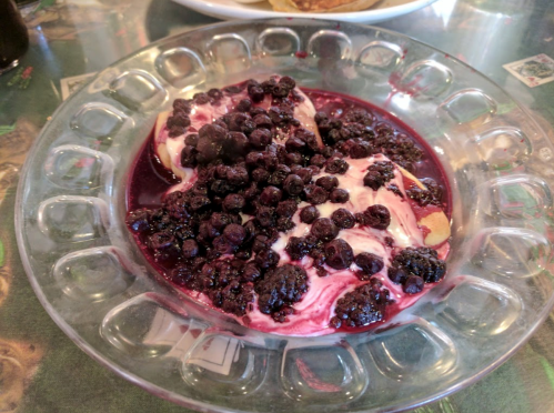 A glass dish filled with creamy dessert topped with a rich layer of dark berry sauce and whole berries.