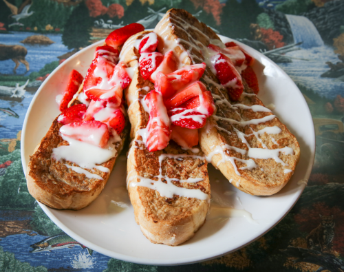 A plate of French toast topped with fresh strawberries and drizzled with cream.
