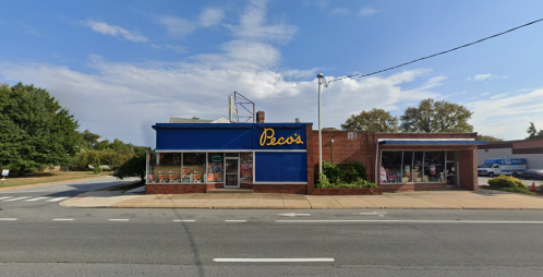 A blue storefront with "Peco's" signage, surrounded by trees and a clear sky, along a quiet street.