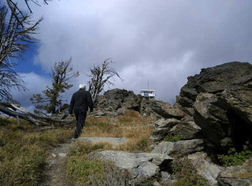 A person walks along a rocky path towards a distant structure under a cloudy sky.