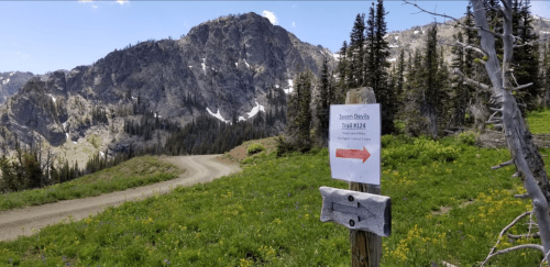 A trail sign points to "Storm Devils Trail 2134" with a dirt path and mountains in the background.