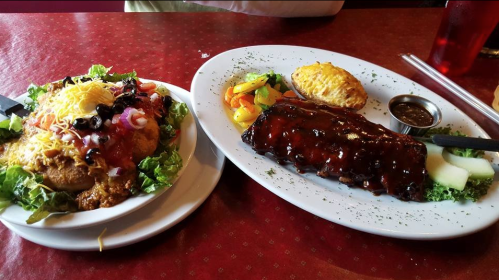 A plate of BBQ ribs with sauce, vegetables, and a biscuit, alongside a salad topped with cheese and salsa.
