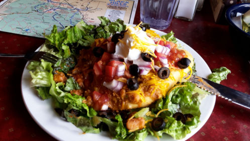 A colorful plate of nachos topped with lettuce, tomatoes, cheese, olives, and sour cream, served on a red table.