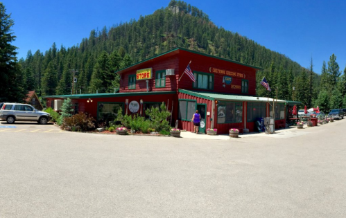 A red building with a sign reading "Store" surrounded by trees and mountains, with a person walking outside.