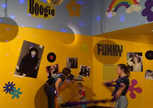 Children and adults dance in a colorful room decorated with music-themed posters and disco elements.