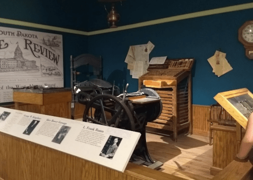 Historic printing press and equipment displayed in a museum, with informational plaques and vintage decor.