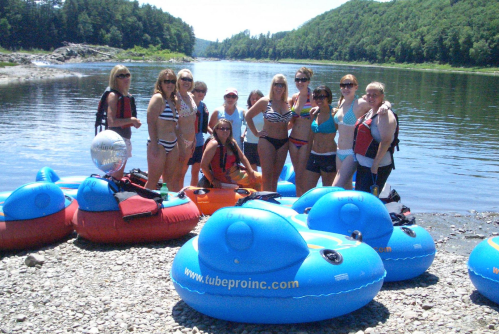 A group of people in swimsuits poses by the river with colorful inflatable tubes on a sunny day.