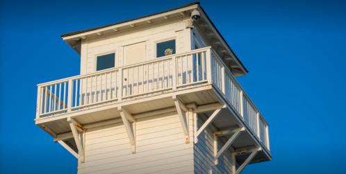 A white lifeguard tower with a balcony against a clear blue sky.
