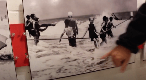Black and white photo of children playing in the ocean, with lifeguards and waves in the background.