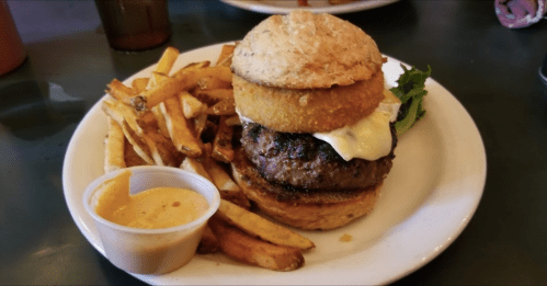A juicy burger with a fried onion ring, lettuce, and cheese, served with crispy fries and a side of mustard.