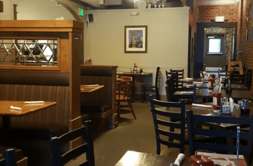 Interior of a cozy restaurant with wooden tables, chairs, and a warm atmosphere, featuring ketchup and mustard on the tables.