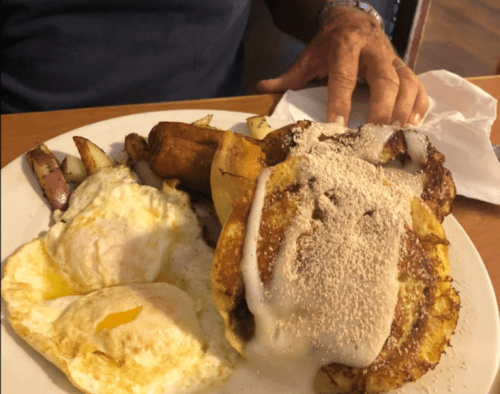 A plate of breakfast featuring two fried eggs, cinnamon roll pancakes, and seasoned potato wedges.