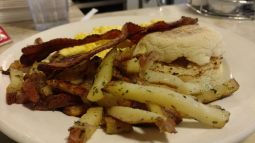 A plate of breakfast featuring scrambled eggs, bacon, and seasoned potato wedges alongside a biscuit.