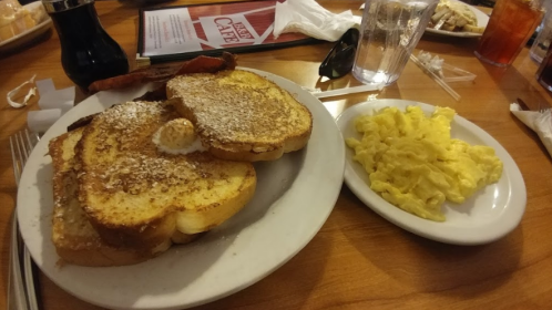 A plate of French toast dusted with powdered sugar and a side of scrambled eggs on a wooden table.