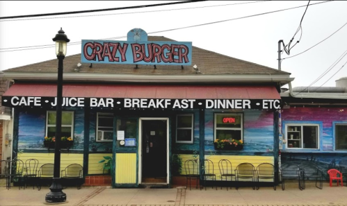 Colorful exterior of "Crazy Burger" restaurant with a sign and outdoor seating, featuring a vibrant mural.