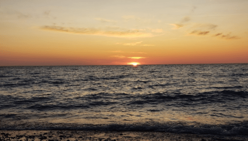 A serene sunset over the ocean, with vibrant orange and pink hues reflecting on the water's surface.