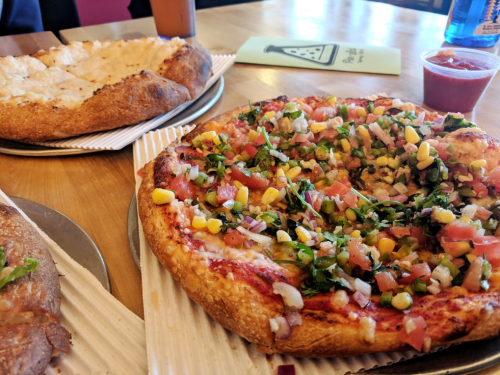 A close-up of two pizzas on a table: one topped with fresh vegetables and the other with a cheesy crust.