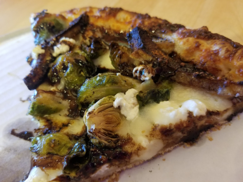 A slice of pizza topped with roasted Brussels sprouts and cheese, featuring a crispy crust.