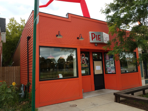 A bright orange restaurant exterior with large windows, featuring a sign that reads "PIE" and a red sculpture above.