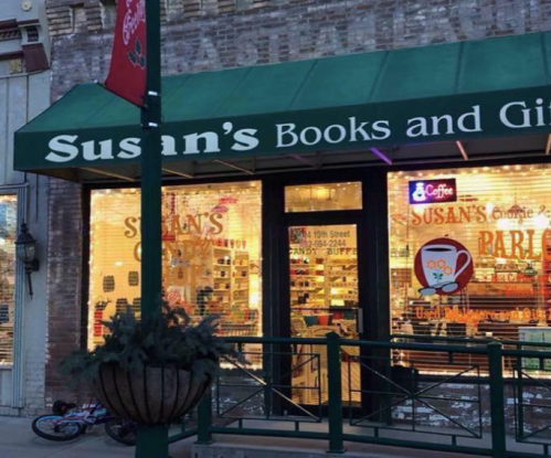 A cozy bookstore and gift shop with a green awning, displaying colorful items in the window, and a festive atmosphere.