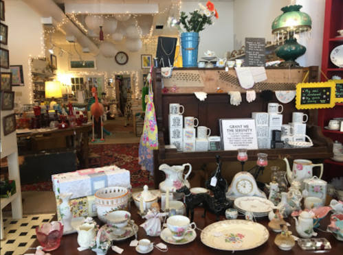 A cozy vintage shop filled with eclectic decor, teacups, and colorful items, illuminated by warm string lights.