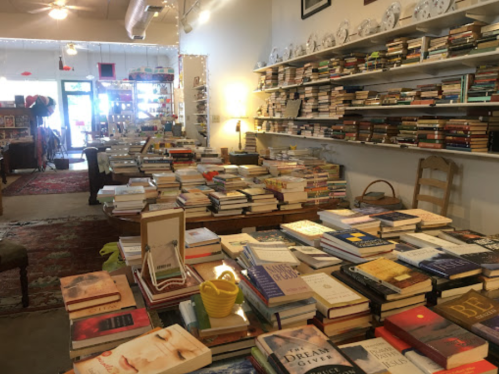 A cozy bookstore interior filled with stacks of books on tables and shelves, with warm lighting and decorative items.
