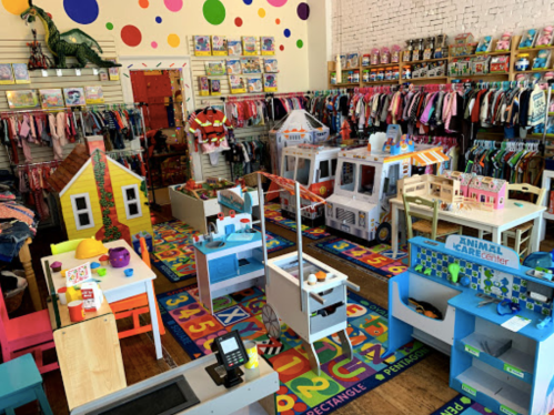 A colorful children's store filled with toys, playsets, and clothing, featuring a vibrant carpet and playful decor.